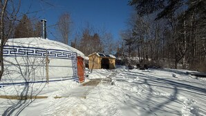 Eine traditionelle Jurte mit Musterdesign, eine Holzkonstruktion in der Nähe und eine verschneite Landschaft mit Bäumen.