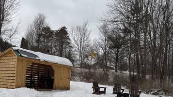 En stuga byggd av trä med ett snötäckt tak, omgiven av ett snöigt landskap och träd utan löv.