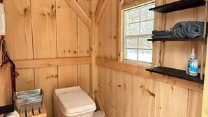 Ein gemütliches Holzhaus mit Toilette, kleinem Fenster und Ablage für eine Flasche.