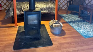 Eine Jurte mit einem zentralen Holzofen, einem Bett mit Felldecke und einem kleinen Tisch mit Stuhl.