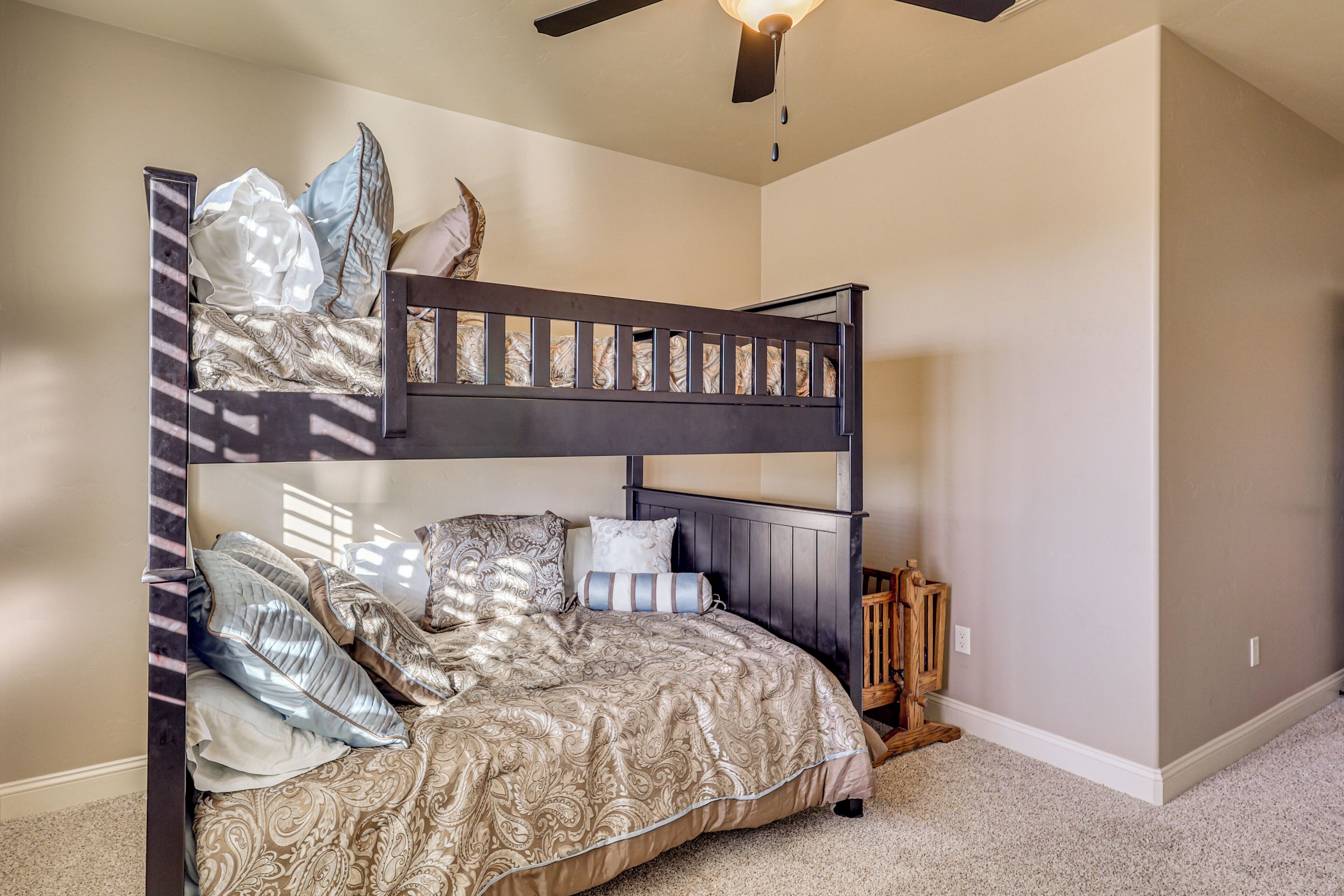 A bunk bed with a patterned bedspread, pillows, and a ceiling fan.