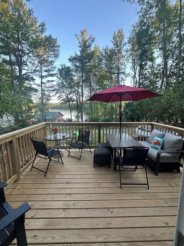 A wooden deck with outdoor furniture, including a table and chairs, and a red umbrella.