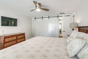 A bedroom with a bed, a dresser, a ceiling fan, a TV mounted on the wall, and a sliding barn-style door. - Hot Tub + Fire Pits: Waterfront Lake Anna Escape! (Louisa)