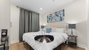 A bedroom with a large bed, a bedside table with a lamp, a painting on the wall, and a curtain. - Modern Styled 2B/2B, Full kitchen, Laundry, Parking (paid) (Toronto)