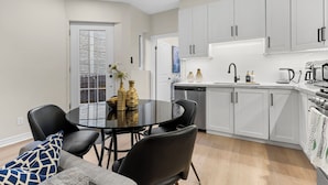 A modern kitchen with white cabinets, a round dining table with chairs, and a view of the adjacent living area. - Modern Styled 2B/2B, Full kitchen, Laundry, Parking (paid) (Toronto)