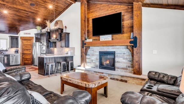 A spacious living area with a stone fireplace, leather sofas, a wooden ceiling, and a kitchen in the background. - Comfort, Convenience, and Room for the Whole Crew (Garden City)
