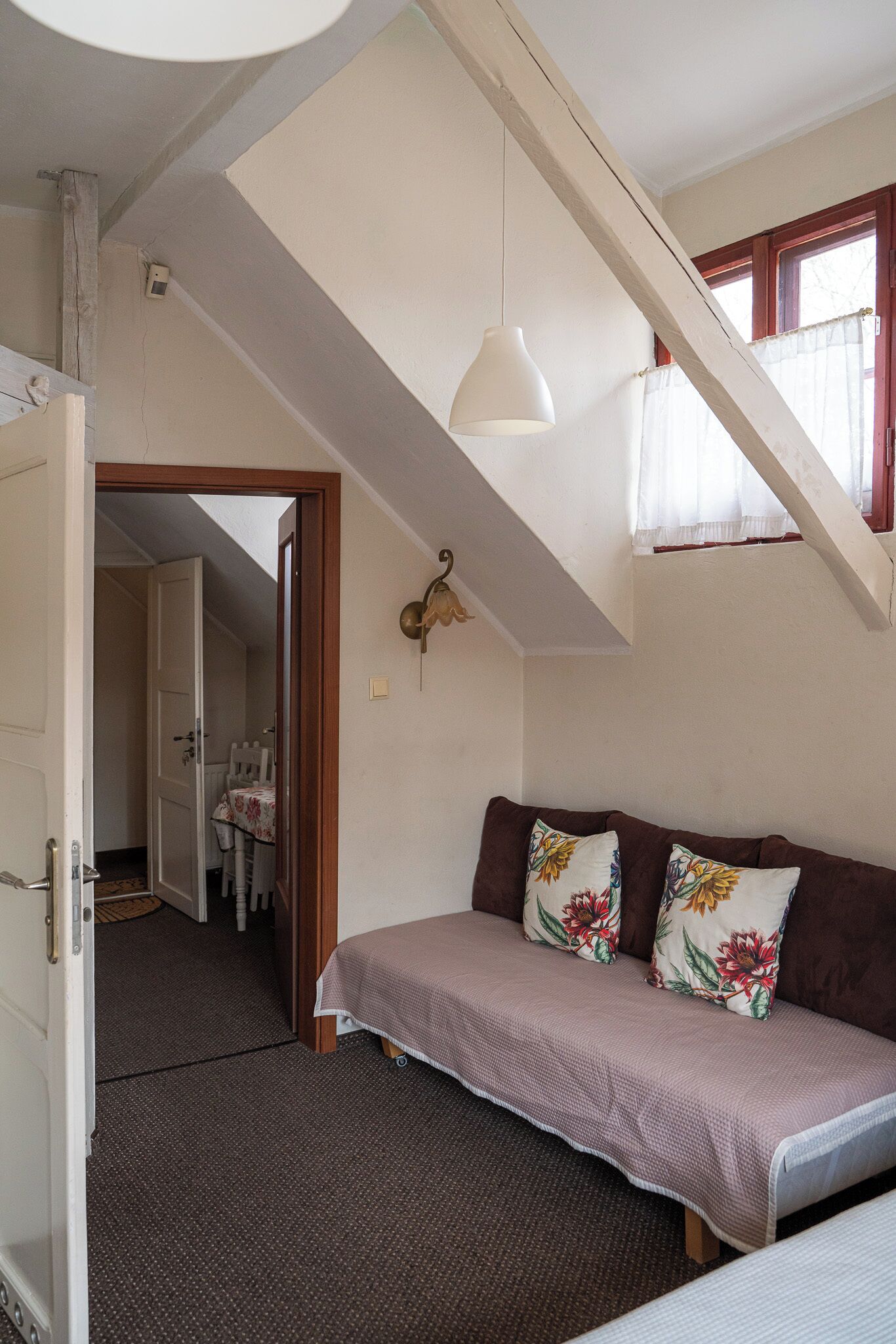 A bedroom with a bed, a wooden bench, a ceiling light, and a window with curtains.