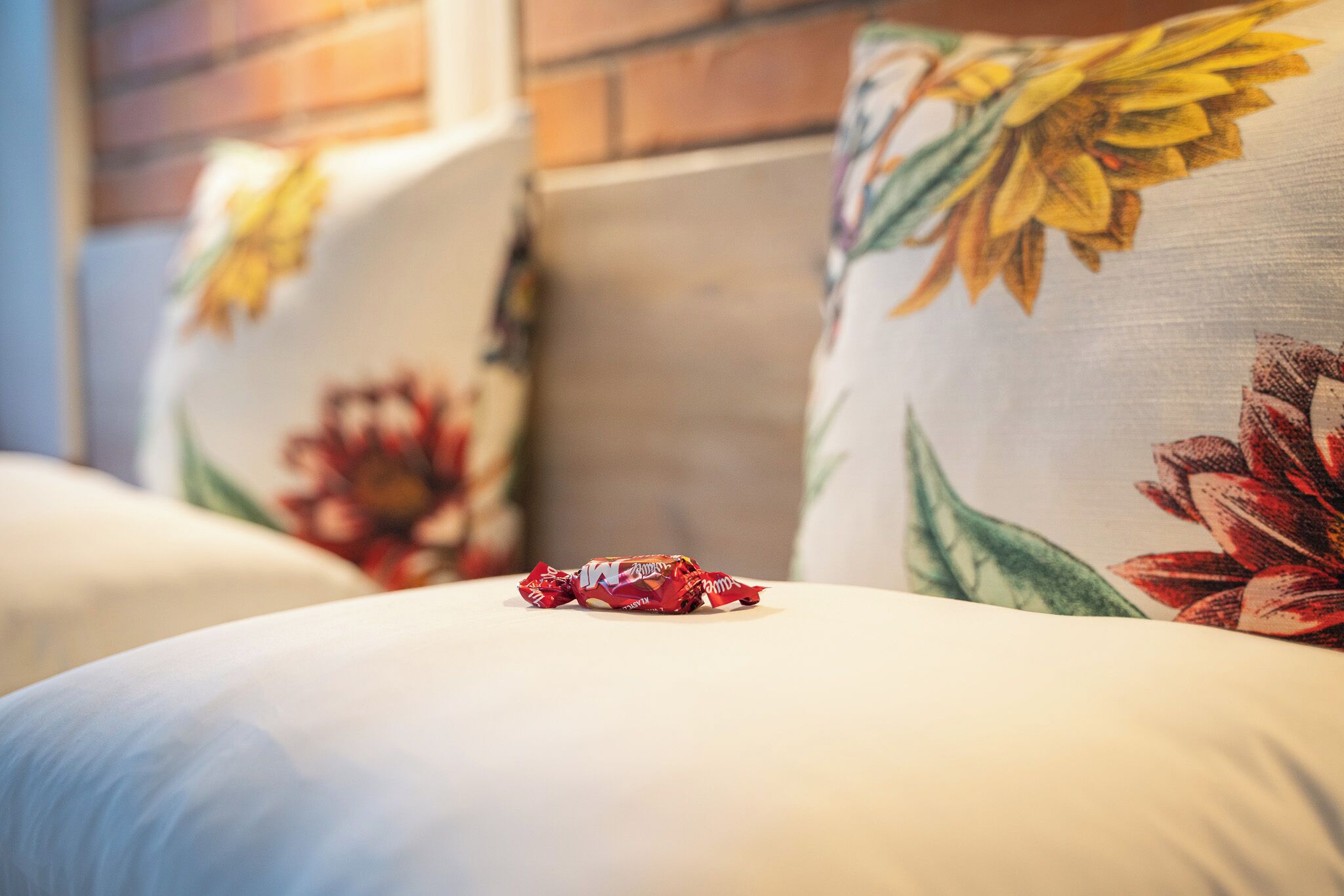 A bed with floral-patterned pillows and a red candy wrapper on the bedspread.
