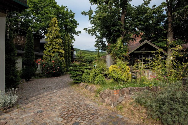 Un sentier pavé de pierres menant à un bâtiment rustique, entouré d’une végétation luxuriante et de plantes en fleurs.