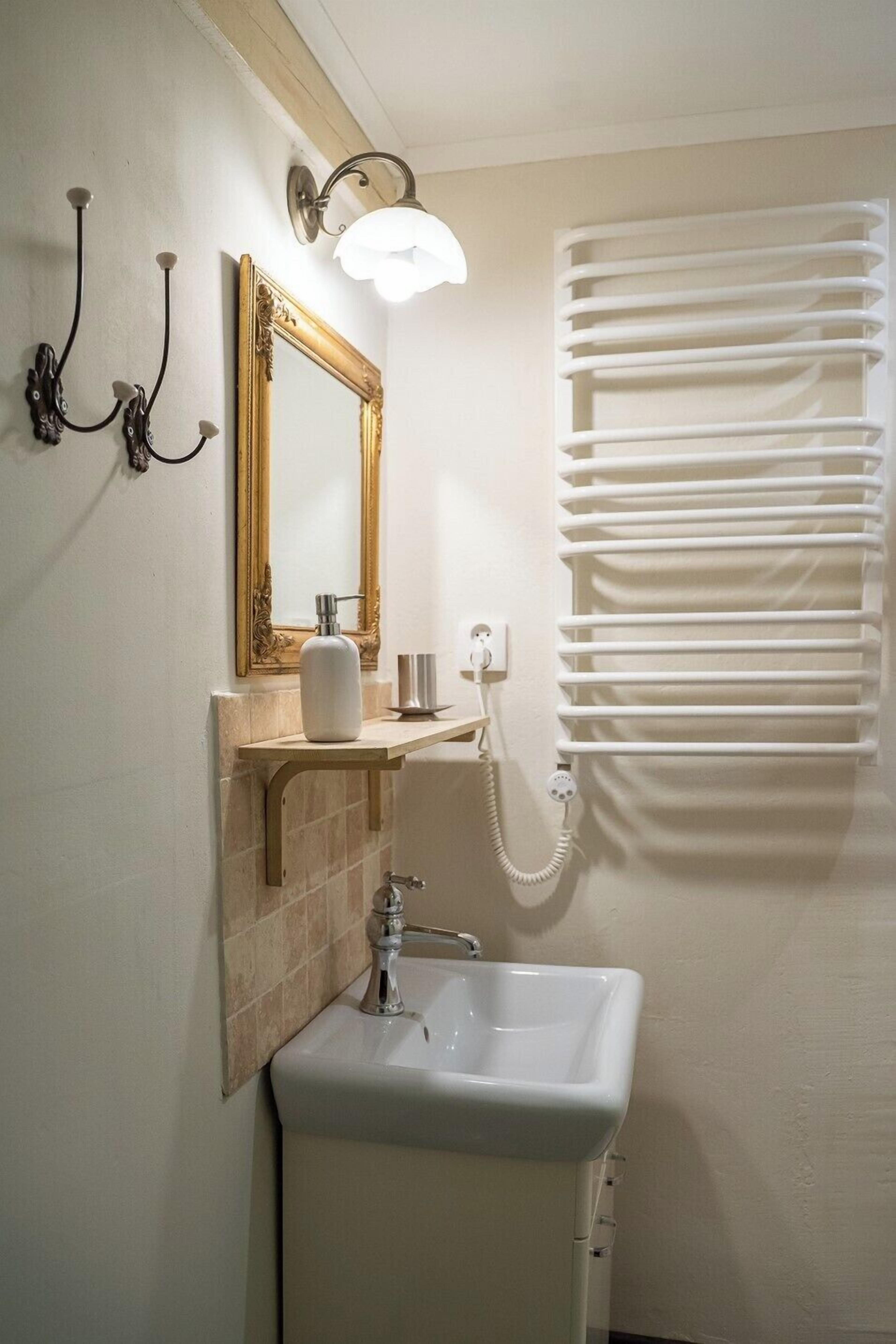 Ein Badezimmer mit einem weißen Waschbecken, einem spiegel mit goldener Rahmung, einer wandmontierten Leuchte und einem Handtuchhalter.