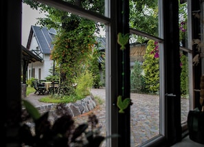 Une cour pavée de pierres, avec un mur en pierre, une clôture en bois et une table entourée de chaises.