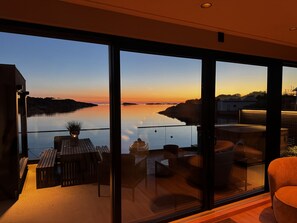 A modern balcony with a glass railing overlooking a calm body of water during sunset.