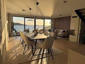 Un comedor moderno con una mesa grande y sillas, un sofá, y vista al mar.