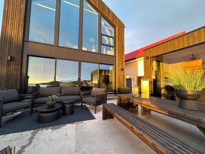 Un área de estar moderna al aire libre con vistas a las montañas, una terraza de madera y un gran edificio de vidrio.