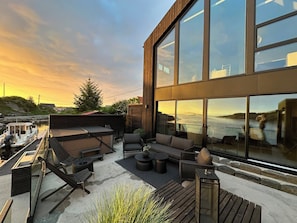 A modern outdoor deck with seating, a view of the water, and a large building with reflective windows.