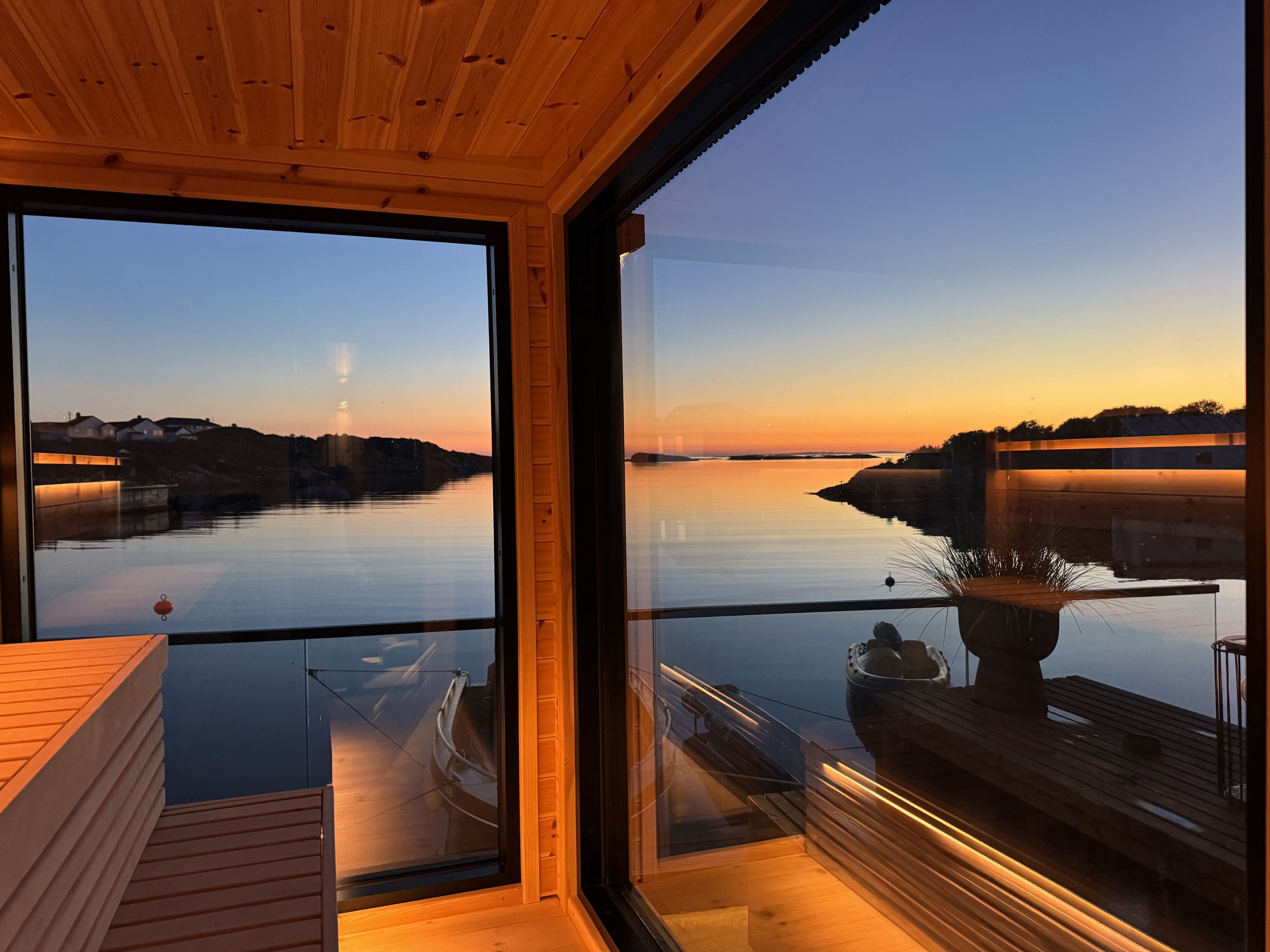 A modern interior with a large glass window overlooking a calm body of water at sunset.