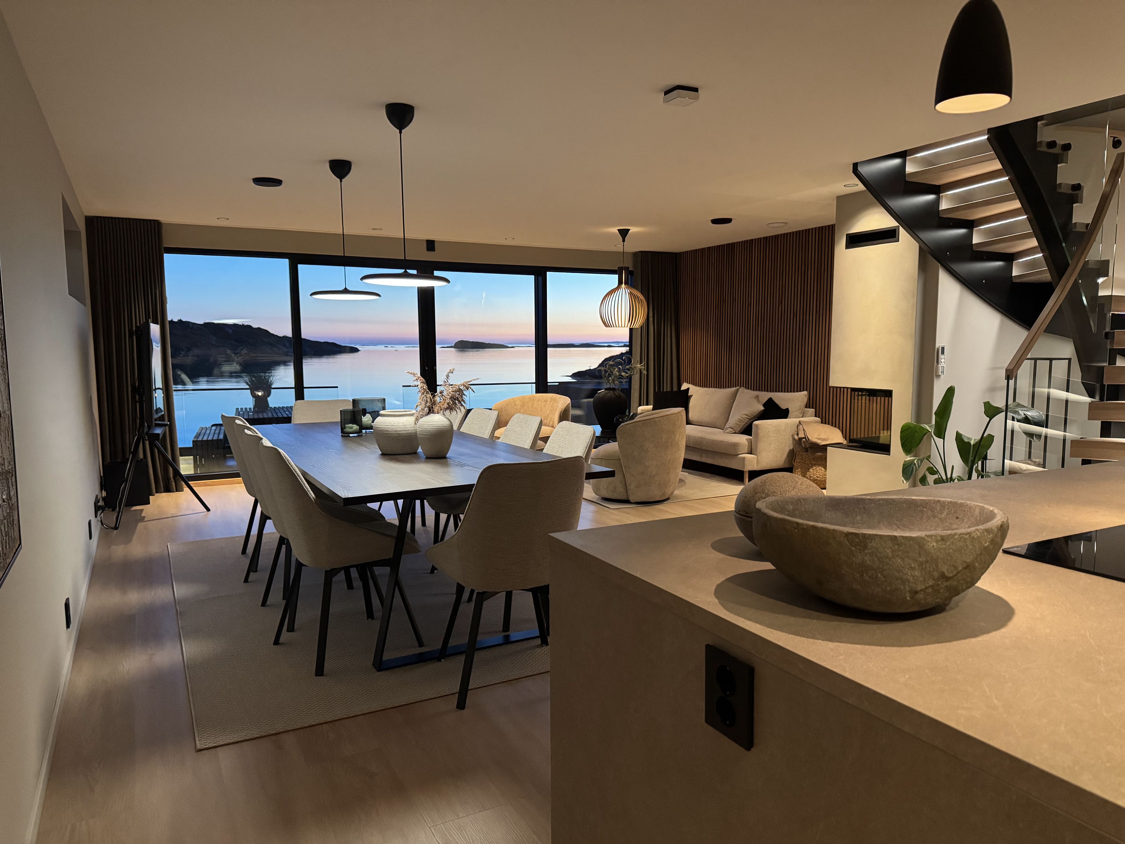 A modern living room with a dining area, large windows, and a view of the water.