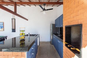 Una cocina con una isla central, armarios azules, encimera negra, ventilador de techo y pared de ladrillo.