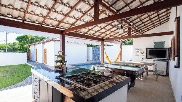 A covered outdoor kitchen with a pool table, a gas stove, and a TV. - QUINTAL DE BÚZIOS
Casa com piscina, churrasqueira, 3 suítes completas com ar (Armação dos Búzios)