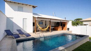 A swimming pool with two lounge chairs and a hammock, a covered outdoor area, and a white building with a tiled roof. - QUINTAL DE BÚZIOS
Casa com piscina, churrasqueira, 3 suítes completas com ar (Armação dos Búzios)