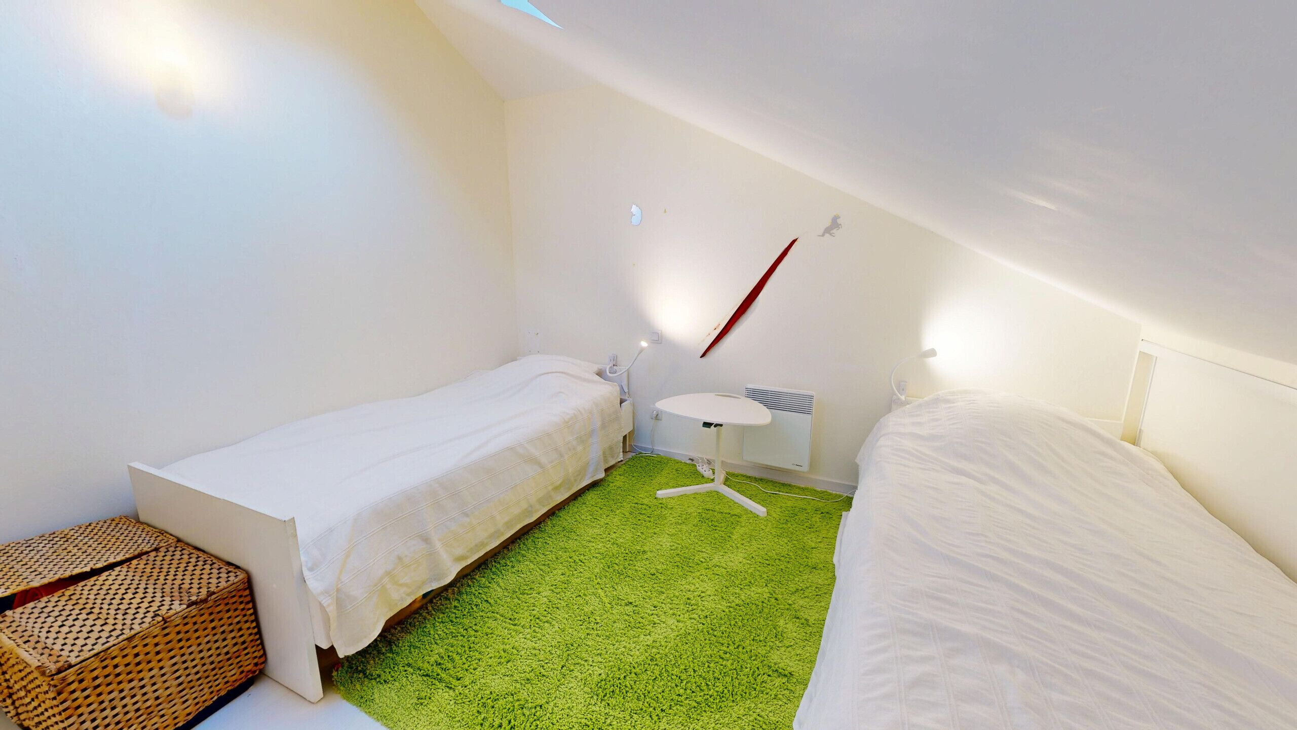 Ein kleines, sauberes Zimmer mit zwei Einzelbetten, einem runden Tisch und einem grünen Teppich.
