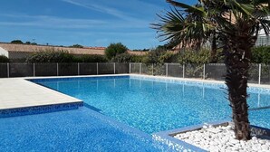 A rectangular swimming pool with clear blue water, surrounded by a white tiled deck and a low white stone border. - Escale Bleu - House with Heated Pool (Notre-Dame-de-Monts)