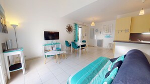 A modern living room with a sofa, a dining area with a table and chairs, a TV mounted on the wall, and a kitchen area with cabinets and a sink. - Escale Bleu - House with Heated Pool (Notre-Dame-de-Monts)