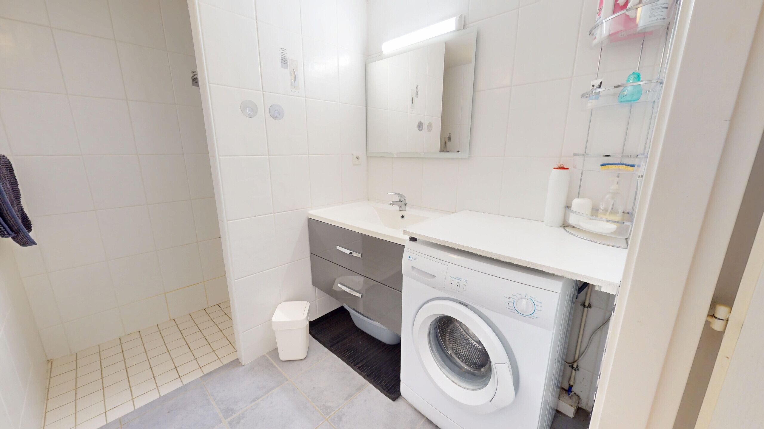 Un bany petit i modern amb un lavabo blanc, un mirall, una rentadora i un vàter.