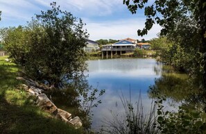 A calm lake with a house on stilts across the water, surrounded by trees and greenery. - Besse Cabin - Air Conditioning, Pools, and Wi-Fi (Saint-Hilaire-de-Riez)