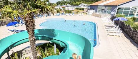 Une piscine avec un toboggan, des chaises longues et un palmier.