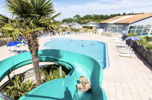 A swimming pool with a water slide, lounge chairs, and a palm tree. - Besse Cabin - Air Conditioning, Pools, and Wi-Fi (Saint-Hilaire-de-Riez)