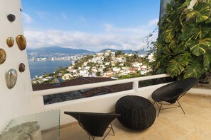 Een balkon met rieten stoelen, uitzicht op een kustplaats, en een decoratieve muur met stenen.