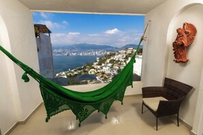 Een kamer met een hangmat, een rieten stoel en uitzicht op een kuststadsgezicht.