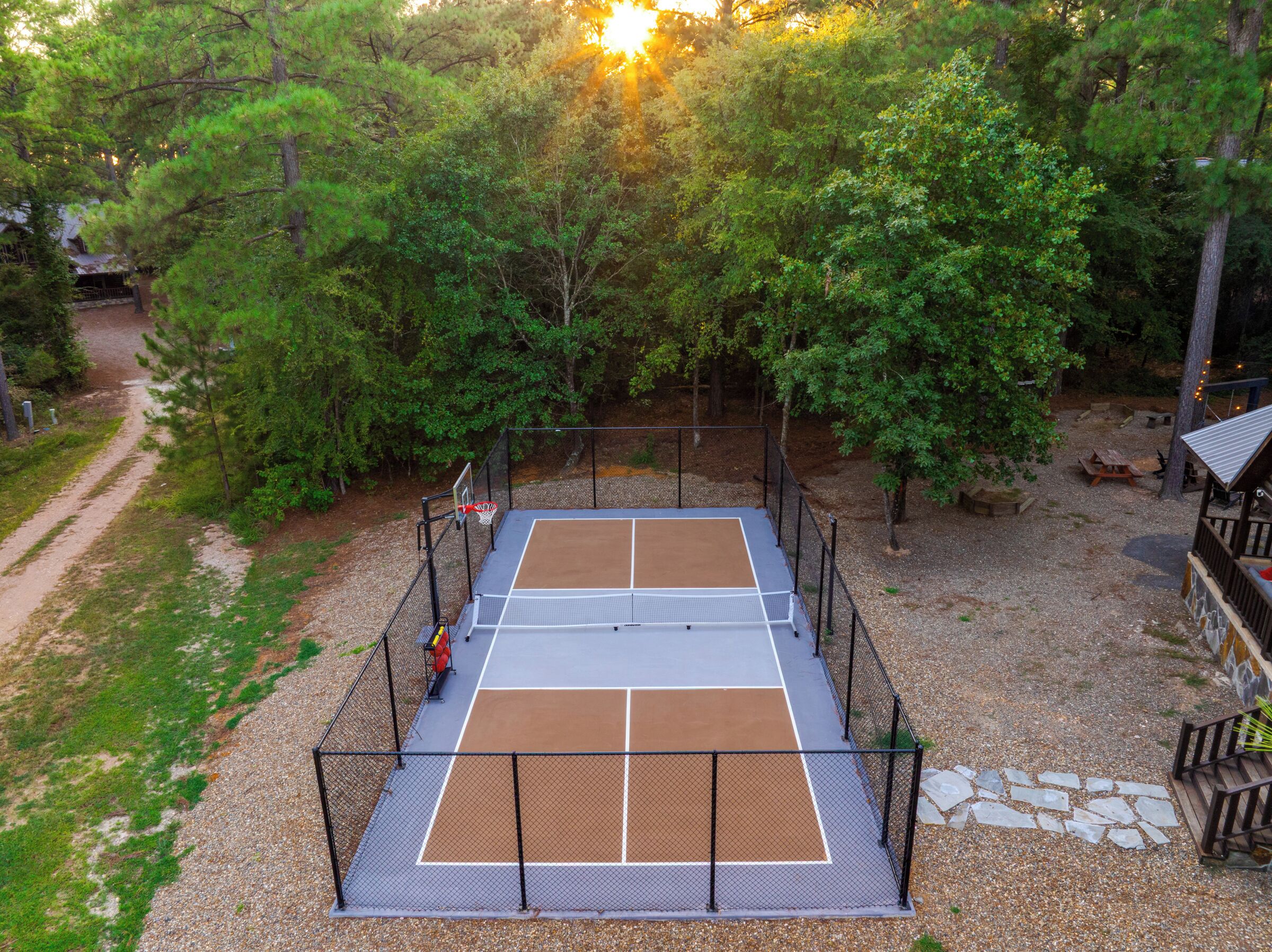 En tennisbana omgiven av träd, med ett staket, bänkar och ett picknickbord.