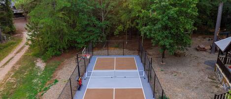 Cancha de tenis rodeada de árboles, con valla, bancos y una mesa de picnic.