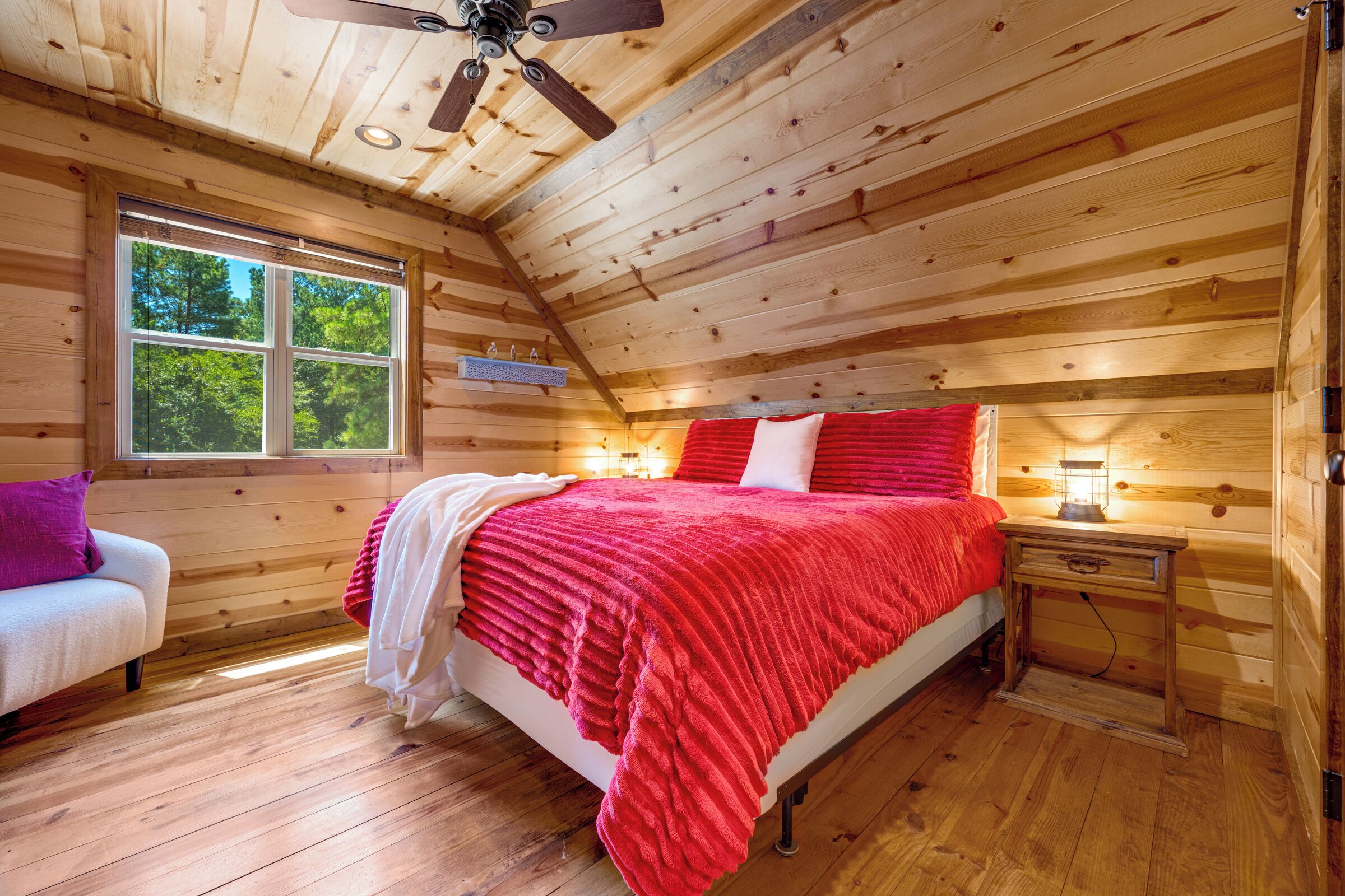 Ein Schlafzimmer einer Holzhütte mit einem Bett, einem Nachttisch, einem Fenster und einem Deckenventilator.