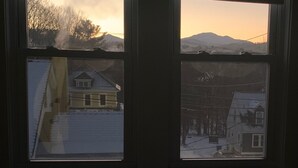A window with a view of a snowy landscape, a mountain in the distance, and a building with a gabled roof. - Littleton: Walk to Downtown, Adventure All Year (Littleton)
