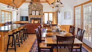 A spacious kitchen with a stone fireplace, wooden ceiling beams, and a large island with bar stools. - North Woods Lodge Vibes•Hot Tub+Fire Pit•3 Seasons Room•Galena Territory Retreat (Galena)