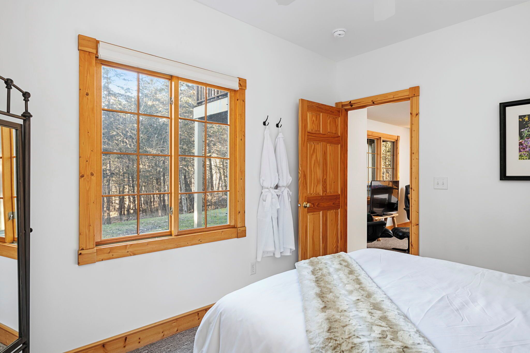 A bedroom with a large window, wooden door, and a bed with a white blanket.