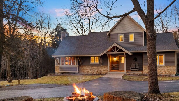 A two-story house with a stone facade, a front porch, and a fire pit in the yard. - North Woods Lodge Vibes•Hot Tub+Fire Pit•3 Seasons Room•Galena Territory Retreat (Galena)