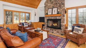 A cozy living room with leather sofas, a stone fireplace, and large windows. - North Woods Lodge Vibes•Hot Tub+Fire Pit•3 Seasons Room•Galena Territory Retreat (Galena)
