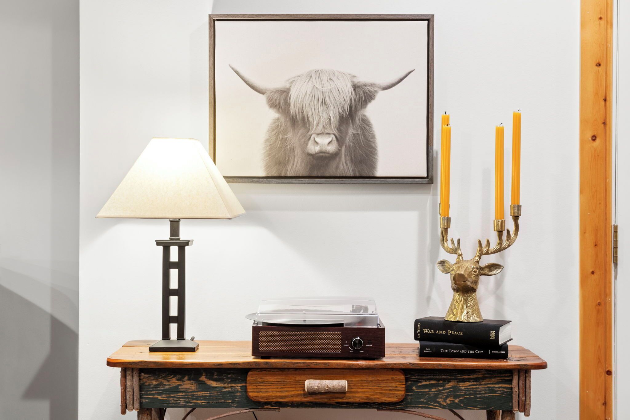 Un tavolo consolle in legno con un giradischi, una fotografia incorniciata di una mucca delle Highlands, una lampada e un candelabro con candele.