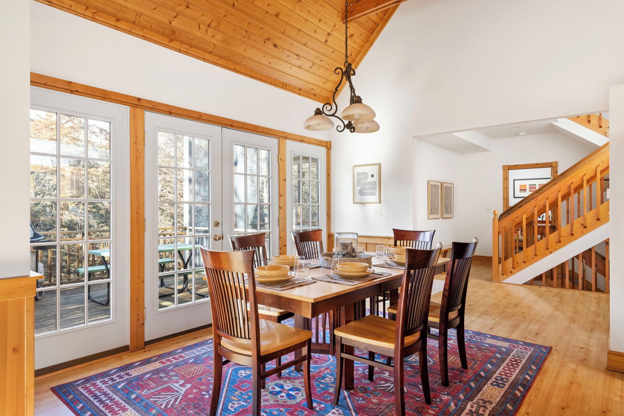 A dining area with a wooden table and chairs, a patterned rug, and a staircase with wooden railings.