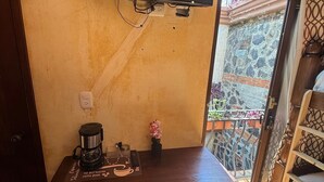 Ein Holztisch mit Kaffeemaschine, ein an der Wand montierter Fernseher und Blick auf einen Balkon mit Geländer und Pflanzen.