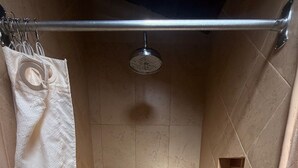 Una ducha con una toalla blanca colgada en un perchero, un cabezal de ducha y una pequeña ventana en la pared.