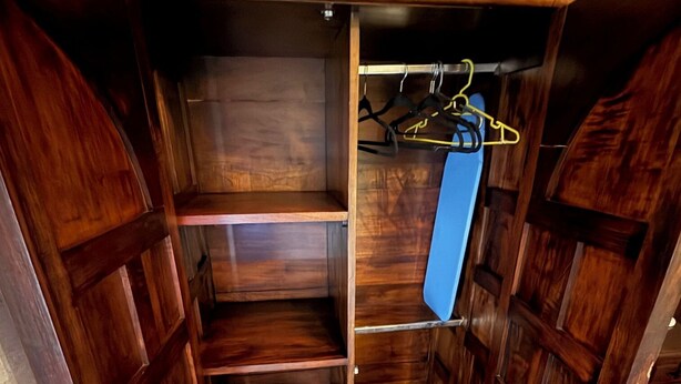 Un vestidor con puertas de madera, varios estantes y una barra colgante azul.