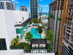 Ein Pool auf dem Dach mit Liegestühlen, umgeben von Grünflächen und modernen Gebäuden.
