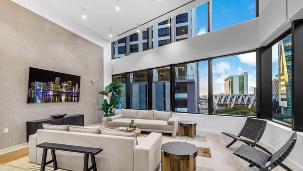 A spacious living area with a modern sofa set, a coffee table, and a bench. Large windows offer a view of the city skyline. - Downtown Miami Studio – Pool, Sauna & Free Parking (Miami)