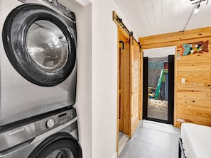 Un espace buanderie équipé d’un lave-linge Samsung, avec des murs en bois et une vue sur un espace de jeux extérieur.