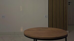 Huoneessa on seinälle asennettu litteänäyttöinen televisio, pyöreä puinen pöytä ja seinässä oleva pystysuora puupaneeli.